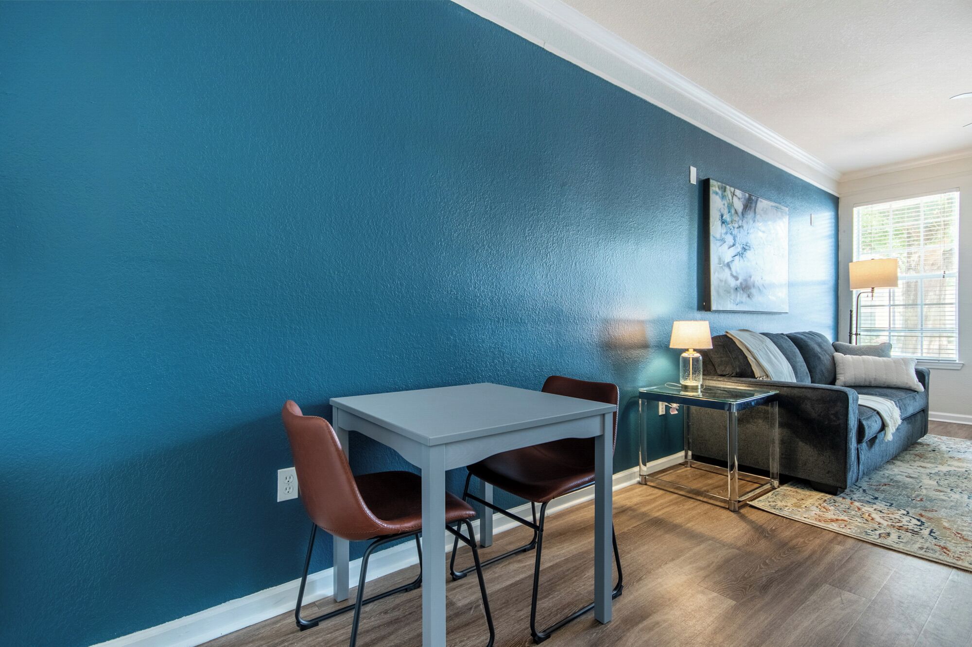 A dining area with a table and chairs, a sofa, and a lamp.