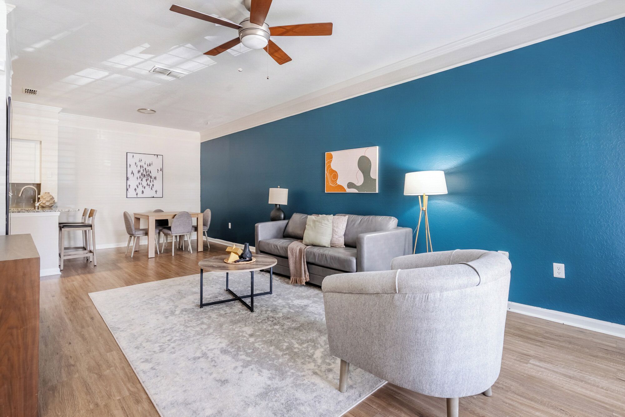 A modern living room with a blue accent wall, a ceiling fan, a grey sofa, a coffee table, and a floor lamp.
