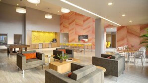 Eine moderne Hotelhalle mit Billardtisch, gemütlicher Sitzgelegenheit, Barbereich und einer Küchenzeile.
