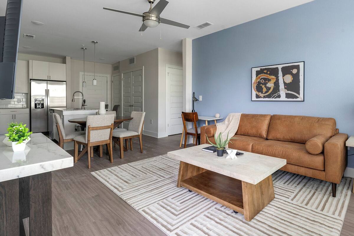 Una sala de estar moderna con un sofá marrón, una mesa de centro y una zona de comedor con sillas y una mesa.