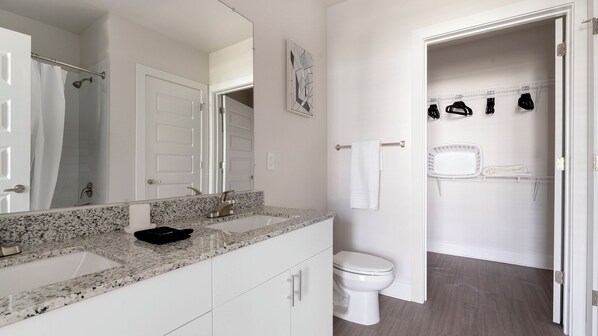 A bathroom with a granite countertop, a white toilet, a shower area, and a towel rack with towels. - Landing Apartments Fort Myers - Cape Coral (Fort Myers)