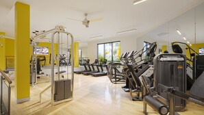 Ein Fitnessstudio mit Laufbändern, Trainingsgeräten und einem Deckenventilator.