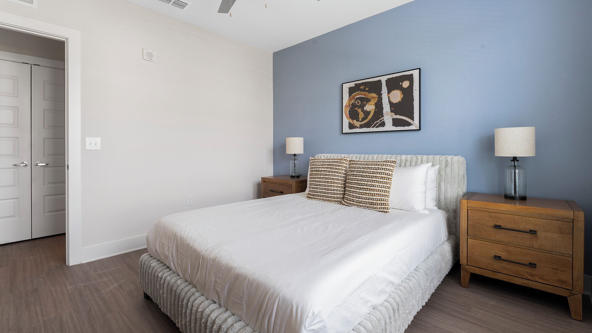 Ein Schlafzimmer mit einem Bett, zwei Nachttischen, einem Wandbild und einer Tür.