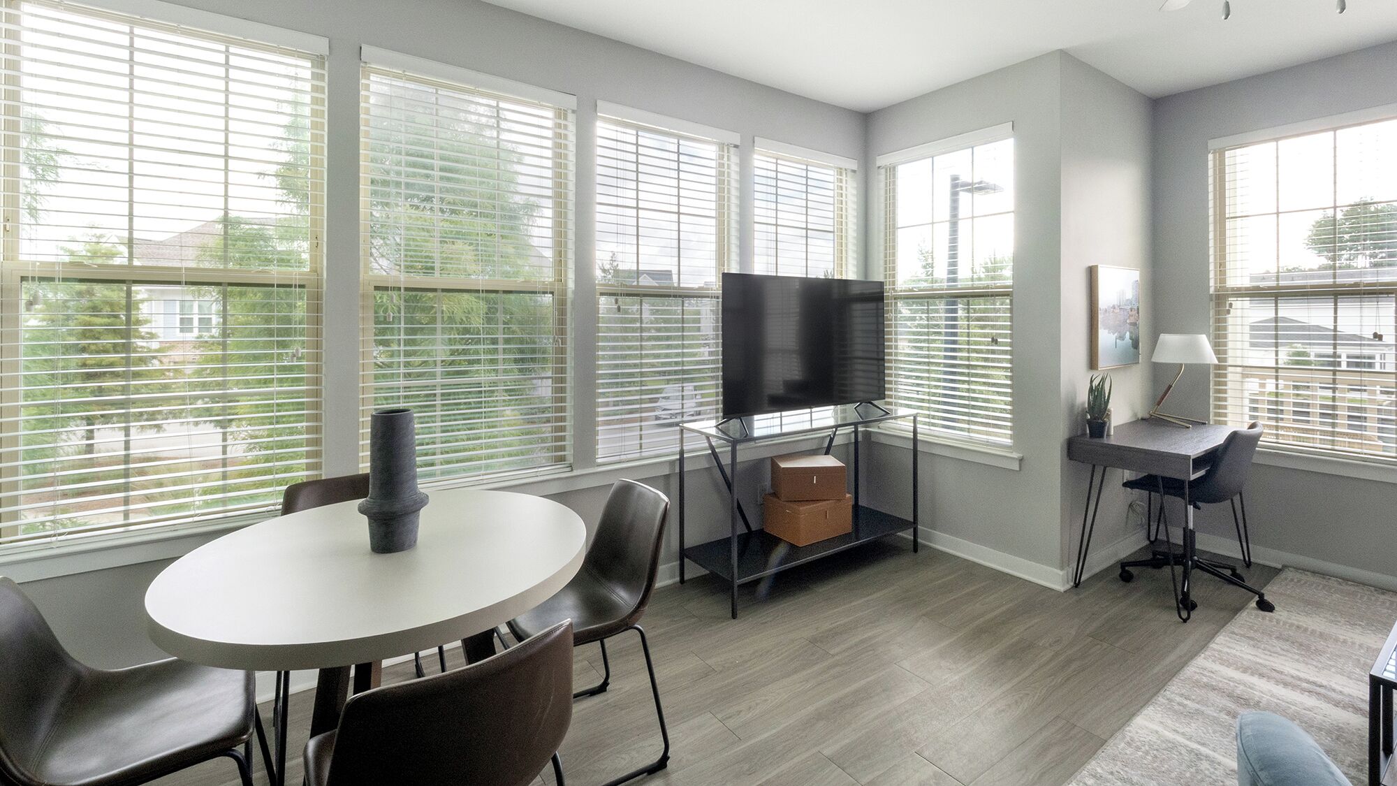 A modern room with large windows, a flat-screen TV, a round table, and a desk with a chair.