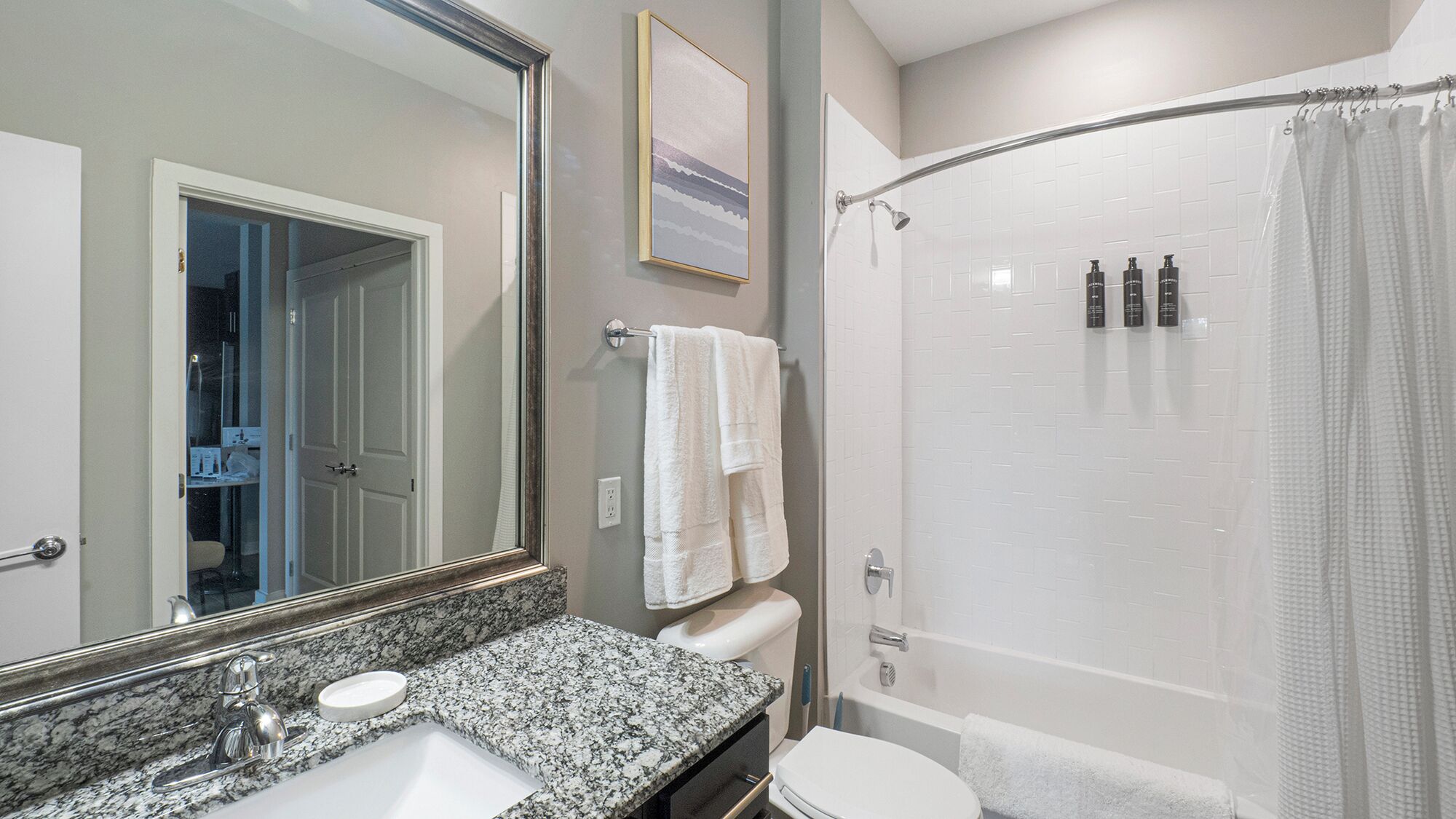 A bathroom with a granite countertop sink, a white toilet, a shower with a glass door, and a large mirror.