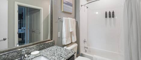 A bathroom with a granite countertop sink, a white toilet, a shower with a glass door, and a large mirror.