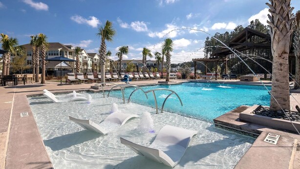A pool area with multiple water features, lounge chairs, and palm trees. - Landing Apartments Charleston - Summerville (Summerville)