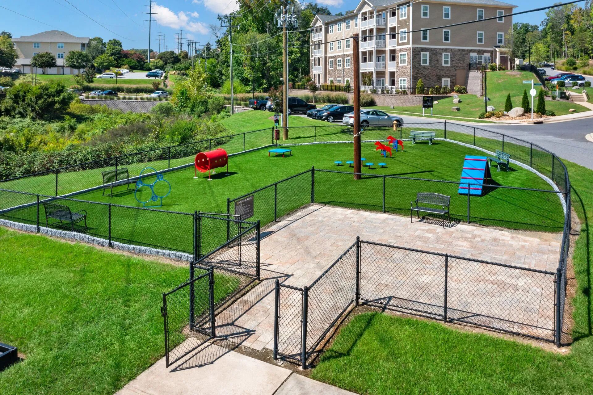 A fenced park with benches, a red barrel, and playground equipment.