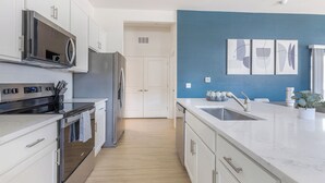 Une cuisine moderne avec des meubles blancs, des appareils en acier inoxydable et un mur d’accent bleu.