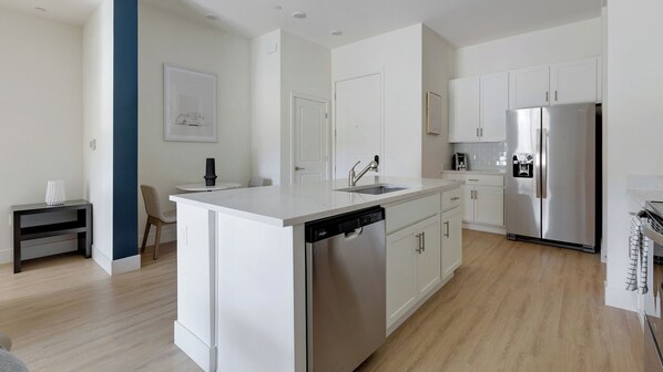 A modern kitchen with white cabinetry, a stainless steel refrigerator, a dishwasher, and a small island with a sink. - Landing Apartments Tucson near La Cholla Professional Park (Tucson)