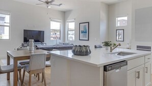 Une cuisine moderne dotée d’un îlot central, un coin repas avec un téléviseur et un espace de vie avec un canapé.