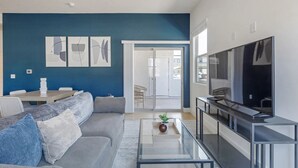 Un salon moderne avec un mur d’accent bleu, un canapé gris, une table basse en verre et un téléviseur à écran plat.
