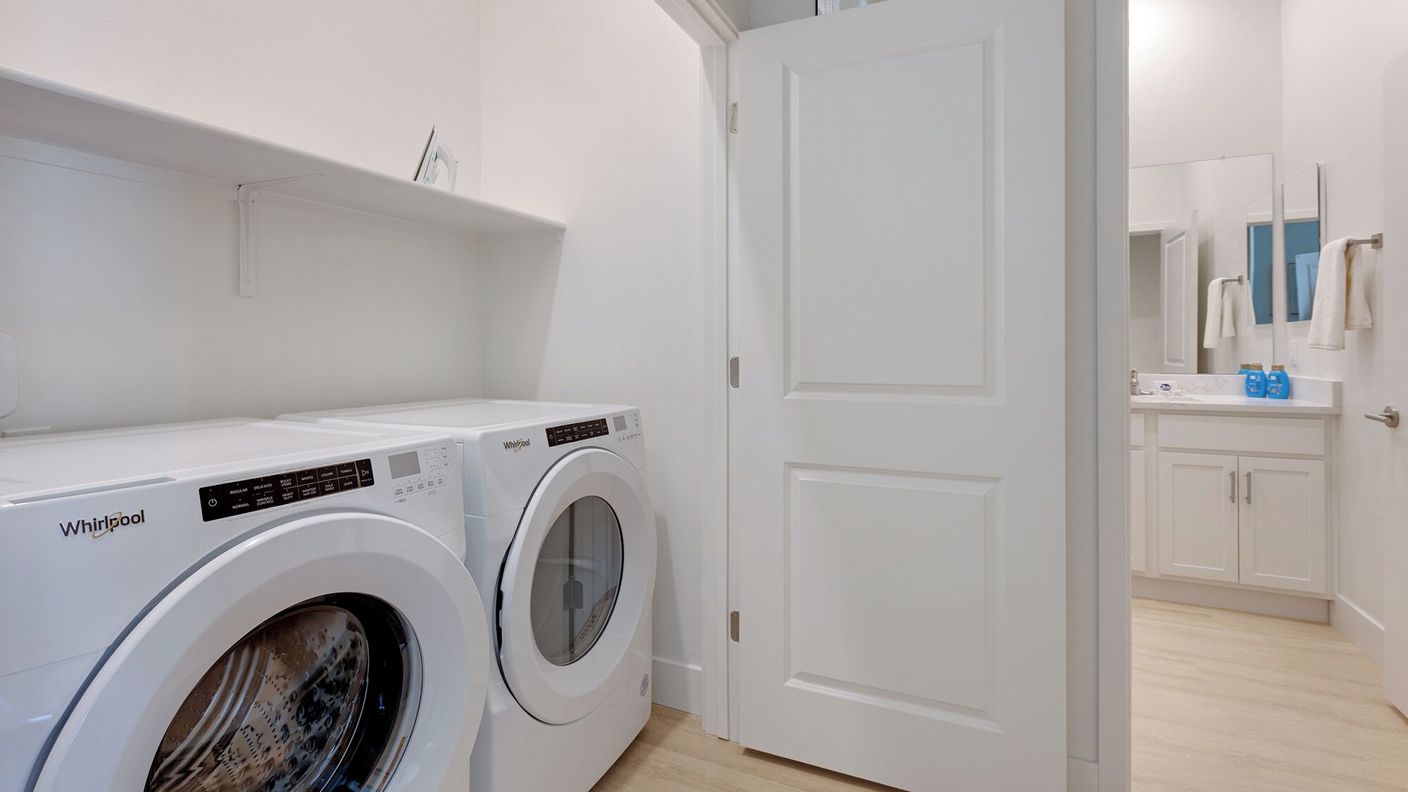 A laundry area with two Whirlpool washing machines, a white door, and a bathroom with a mirror and sink.