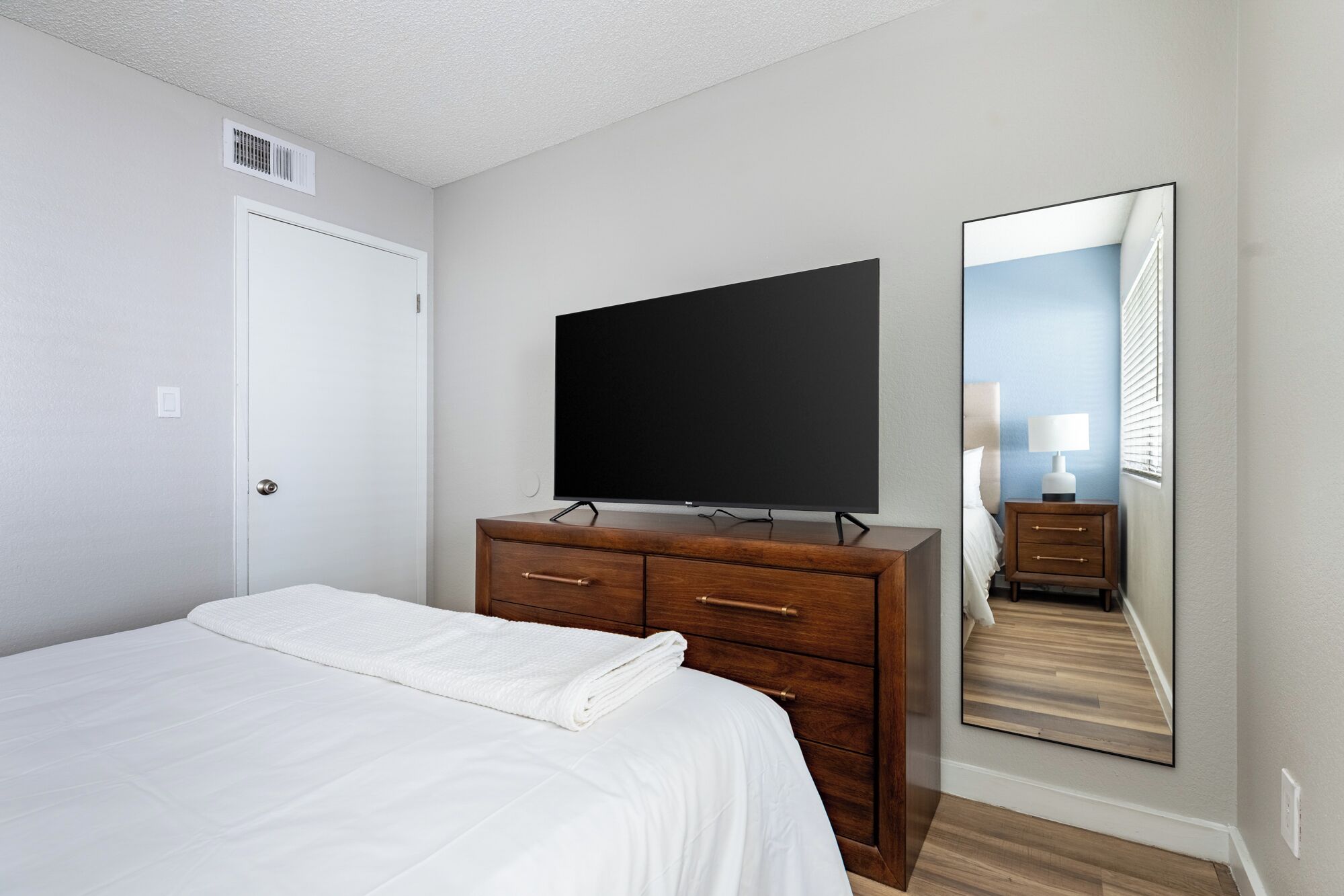 A bedroom with a bed, a dresser, a television, and a large mirror.