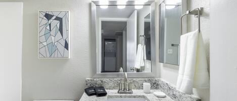 A modern bathroom with a granite countertop sink, a large mirror, and a geometric art piece on the wall.