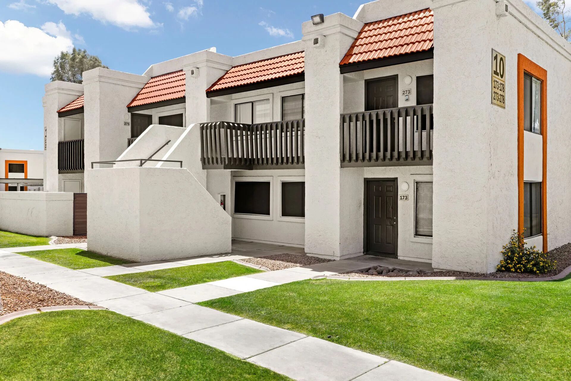 A modern multi-story building with balconies, numbered units, and a well-maintained lawn.