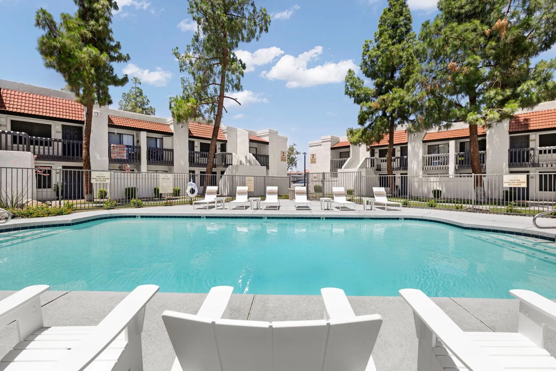 A swimming pool with white lounge chairs and a building with balconies and a tiled roof.