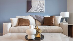 Un salon comprenant un canapé, des coussins, une table basse, une lampe et une œuvre d’art murale.