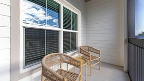 Een hoek van een kamer met twee rieten stoelen en een groot raam met zonwering.