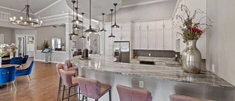 A modern kitchen with a curved island, bar stools, pendant lighting, and a stainless steel refrigerator.