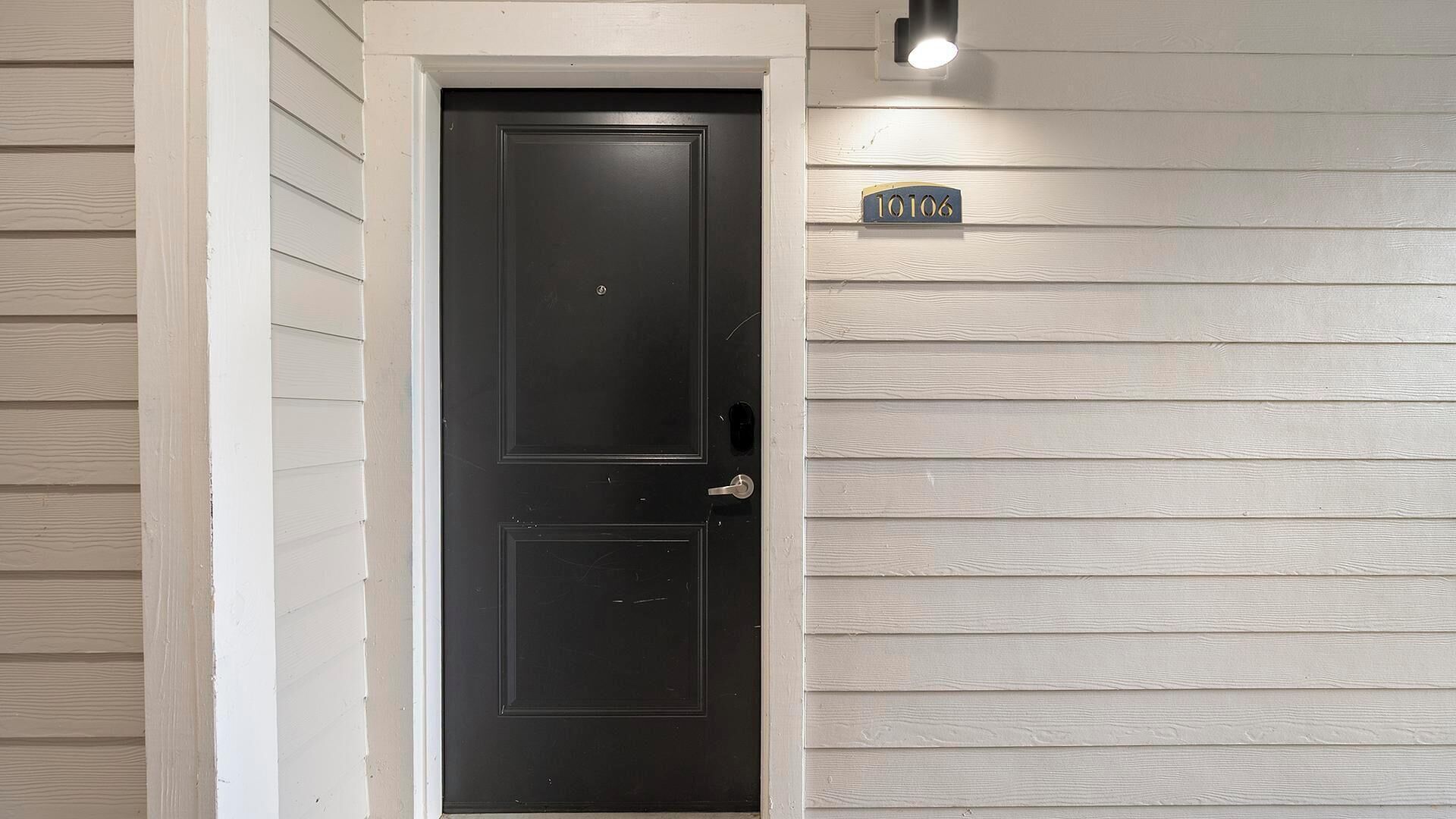 A black door with a small window, a light fixture above it, and a house number sign on the wall.