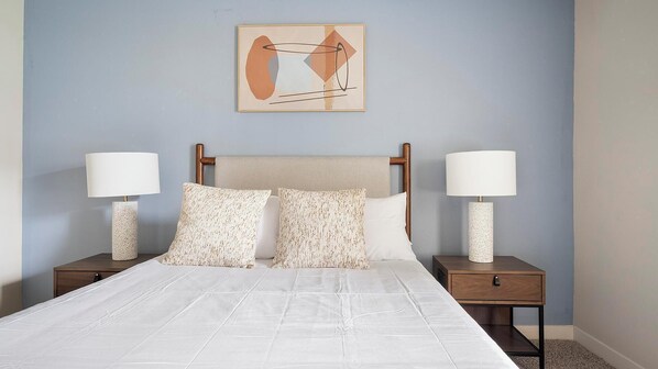A neatly made bed with a white duvet, two matching pillows, and two bedside tables with lamps.