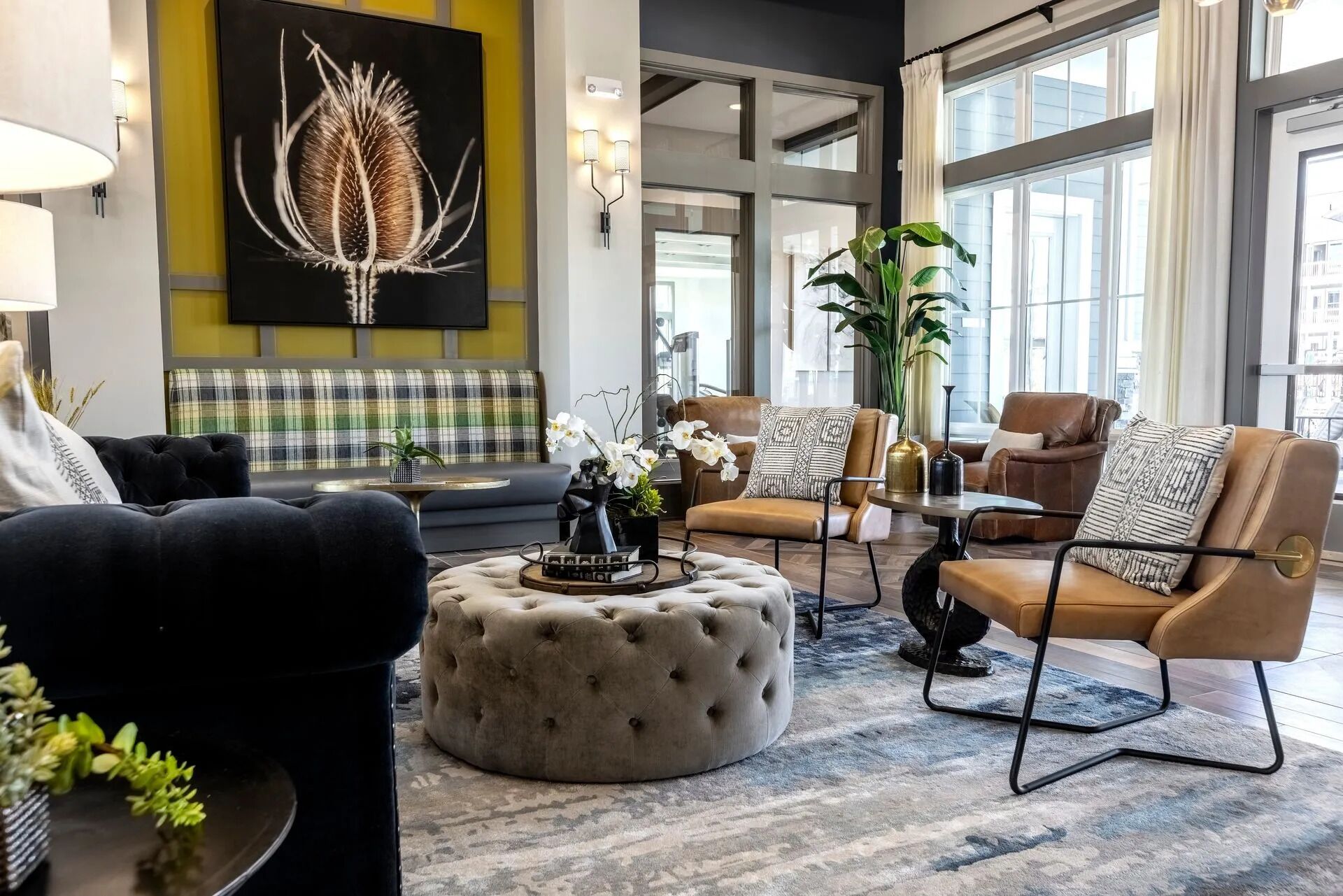 Un salon moderne comprenant un canapé, des fauteuils et un pouf, agrémenté d’une grande fenêtre, d’œuvres d’art et d’une plante en pot.