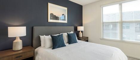 A bedroom with a bed, two bedside tables, a ceiling fan, a window with blinds, and a framed picture on the wall.