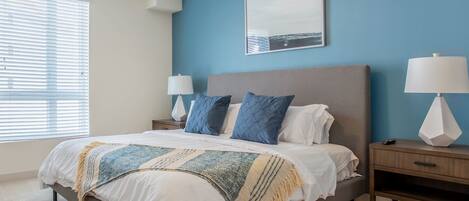 A bedroom with a large bed, two bedside tables, a nightstand, a wall-mounted lamp, and a framed picture.