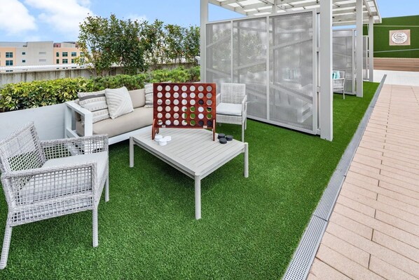 A patio area with a white sofa, two wicker chairs, a wooden coffee table, and a decorative screen. - Landing Apartments Orlando - Central Business District (Orlando)