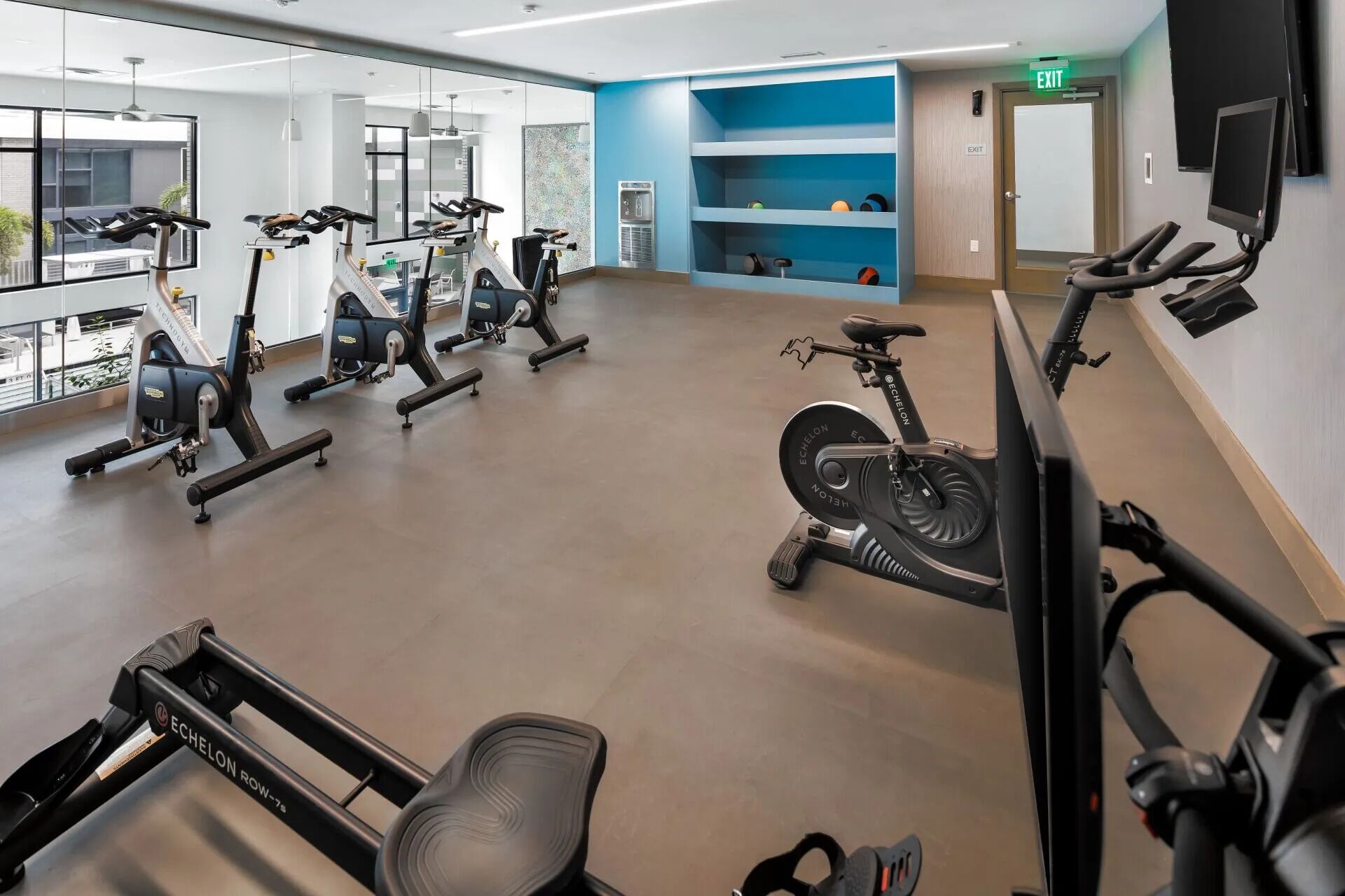 A gym with multiple cardio machines, a water dispenser, and a blue wall with shelves.