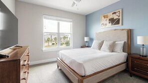 A bedroom with a bed, a TV, a window, and a painting on the wall. - Landing Apartments Jacksonville - Downtown Saint Johns (St. Johns)