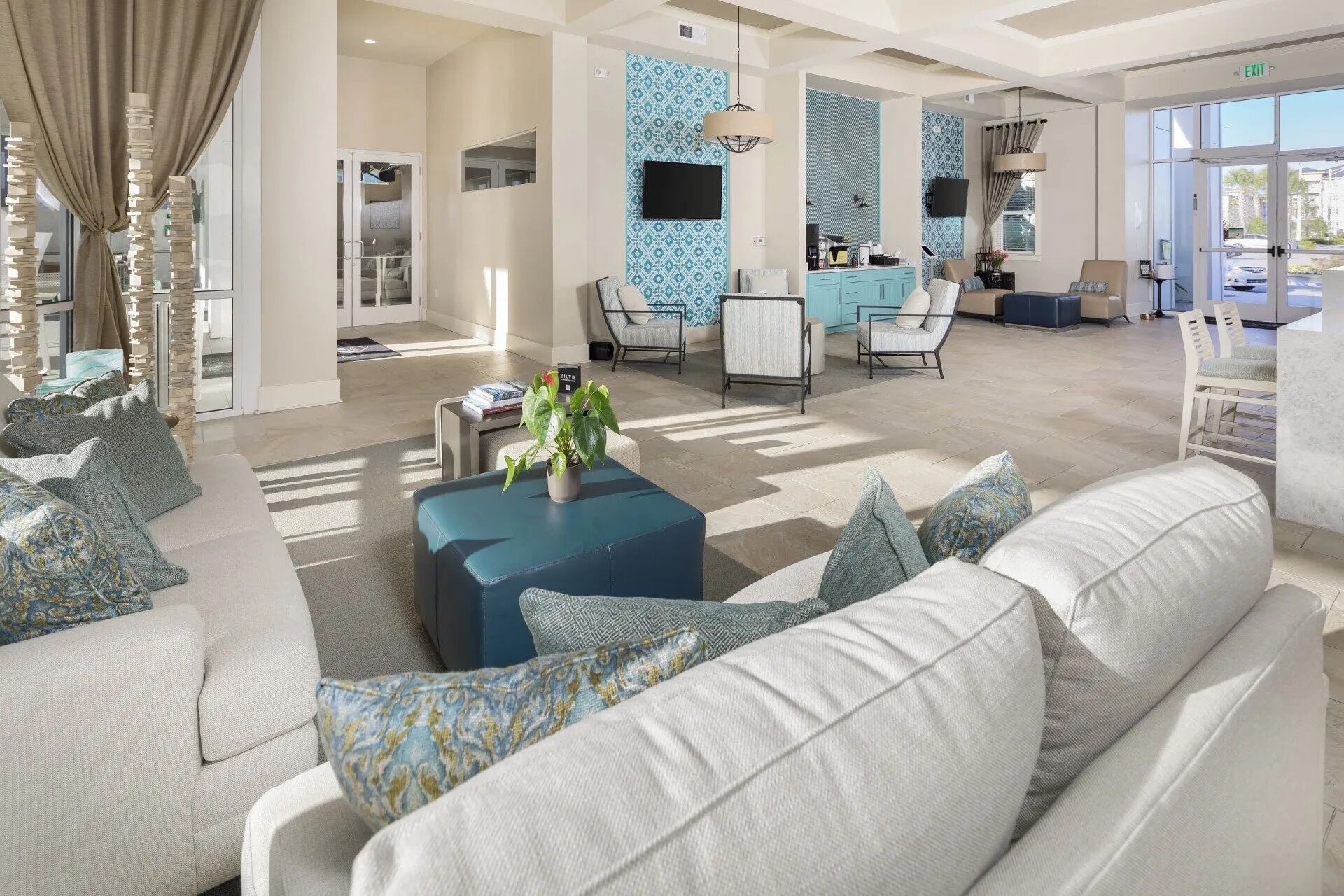 A spacious lobby with a modern design, featuring a seating area with sofas and armchairs, a coffee station, and a television mounted on the wall.