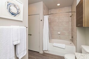 A modern bathroom with a bathtub, shower, and toilet. There are white towels on the floor and a shower curtain. - Landing Apartments - Indian Trail (Indian Trail)