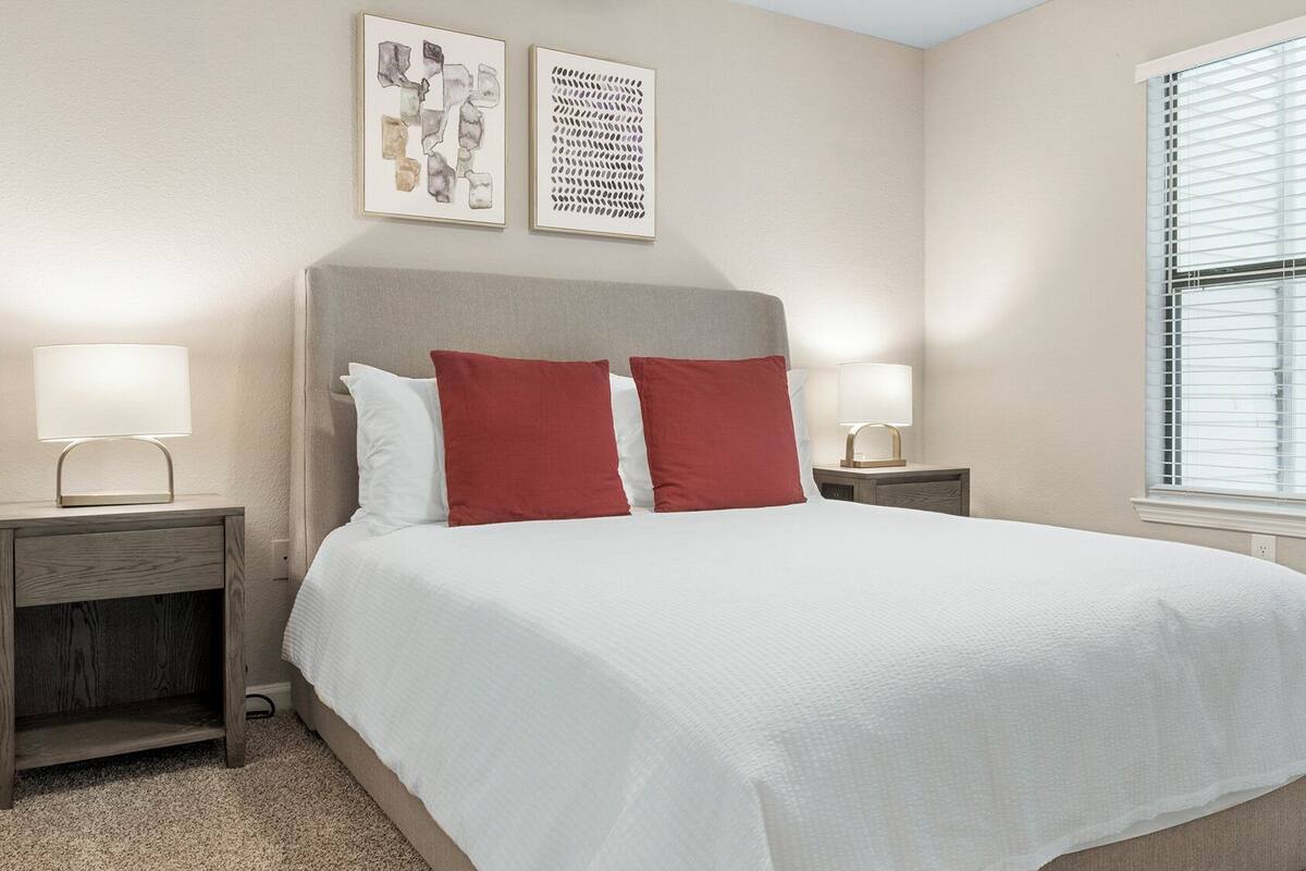A neatly arranged bedroom with a large bed, two nightstands, and a window with blinds.