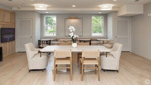 A spacious dining area with a long table and six chairs, surrounded by large windows and a decorative wall piece.