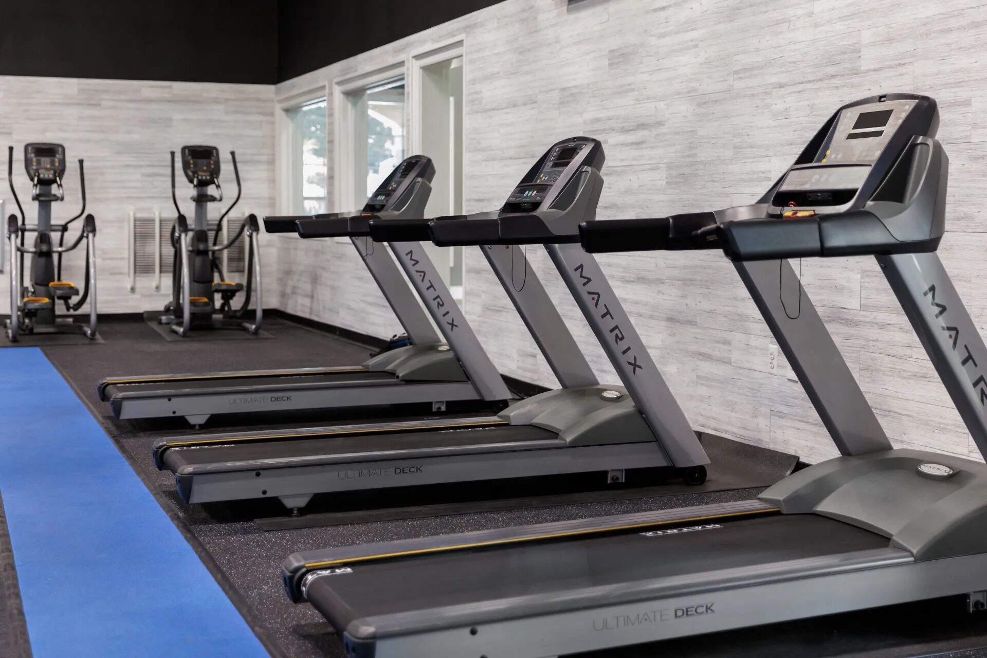 A row of treadmills labeled "MATRIX" in a gym with a blue mat and white walls.