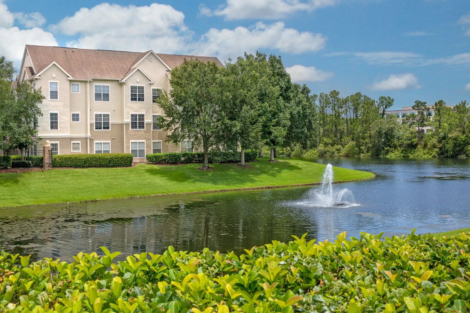 A multi-story building with a flat roof, surrounded by a well-maintained lawn and a body of water with a fountain.