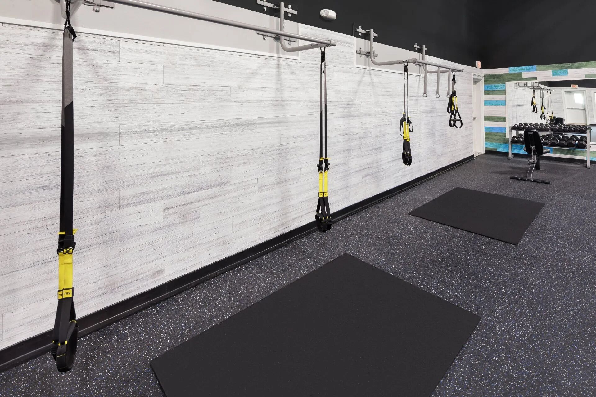 A gym with TRX suspension straps, weight plates, and a black mat.
