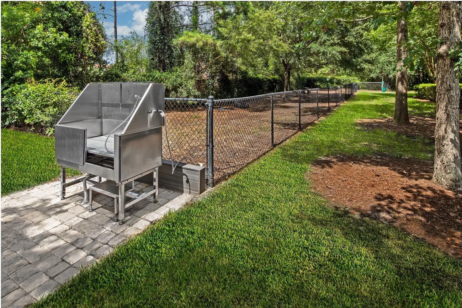 A portable grill in a park with a chain-link fence and trees in the background.