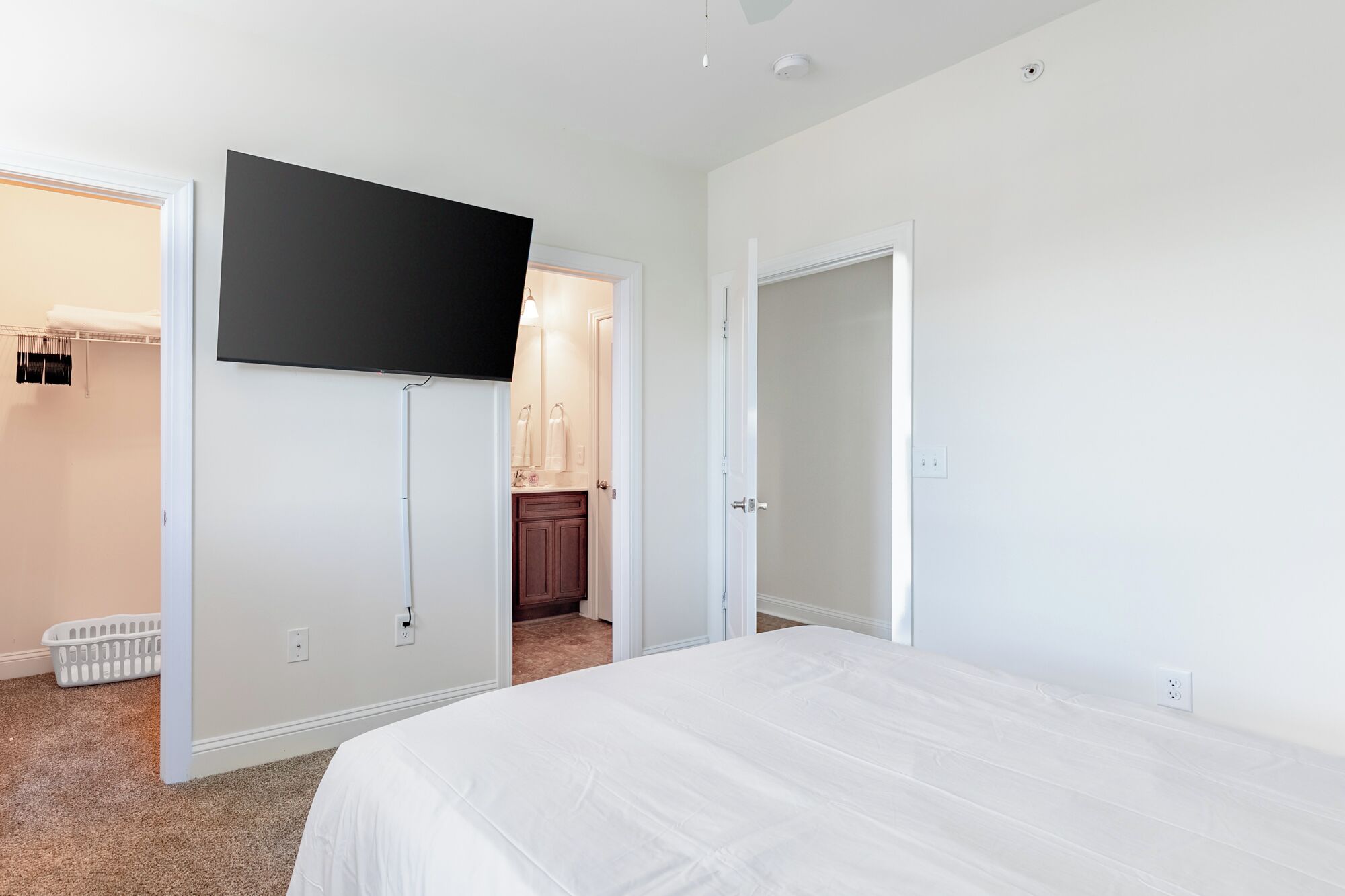 A bedroom with a bed, a TV mounted on the wall, a closet, and a bathroom visible through an open door.