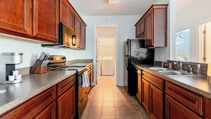 A kitchen with wooden cabinets, stainless steel appliances, and a tiled floor. - Landing Apartments Myrtle Beach - Carolina Forest (Myrtle Beach)