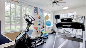 A gym with exercise equipment, large windows, and a ceiling fan. - Landing Apartments Myrtle Beach - Carolina Forest (Myrtle Beach)