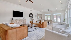 A spacious living room with a modern design, featuring a large TV, comfortable seating, and a ceiling fan. - Landing Apartments Myrtle Beach - Carolina Forest (Myrtle Beach)