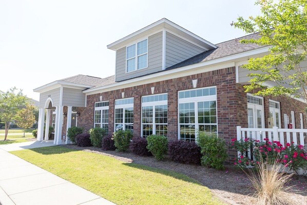 A two-story building with a brick facade, large windows, and a white picket fence. - Landing Apartments Myrtle Beach - Carolina Forest (Myrtle Beach)