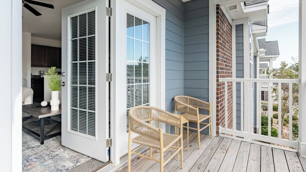 A covered porch with two wicker chairs, a white door, and a view of a residential area. - Landing Apartments Myrtle Beach - Carolina Forest (Myrtle Beach)