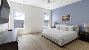 Quarto com uma cama grande, duas mesas de cabeceira, um criado-mudo, um ventilador de teto e duas janelas com persianas.