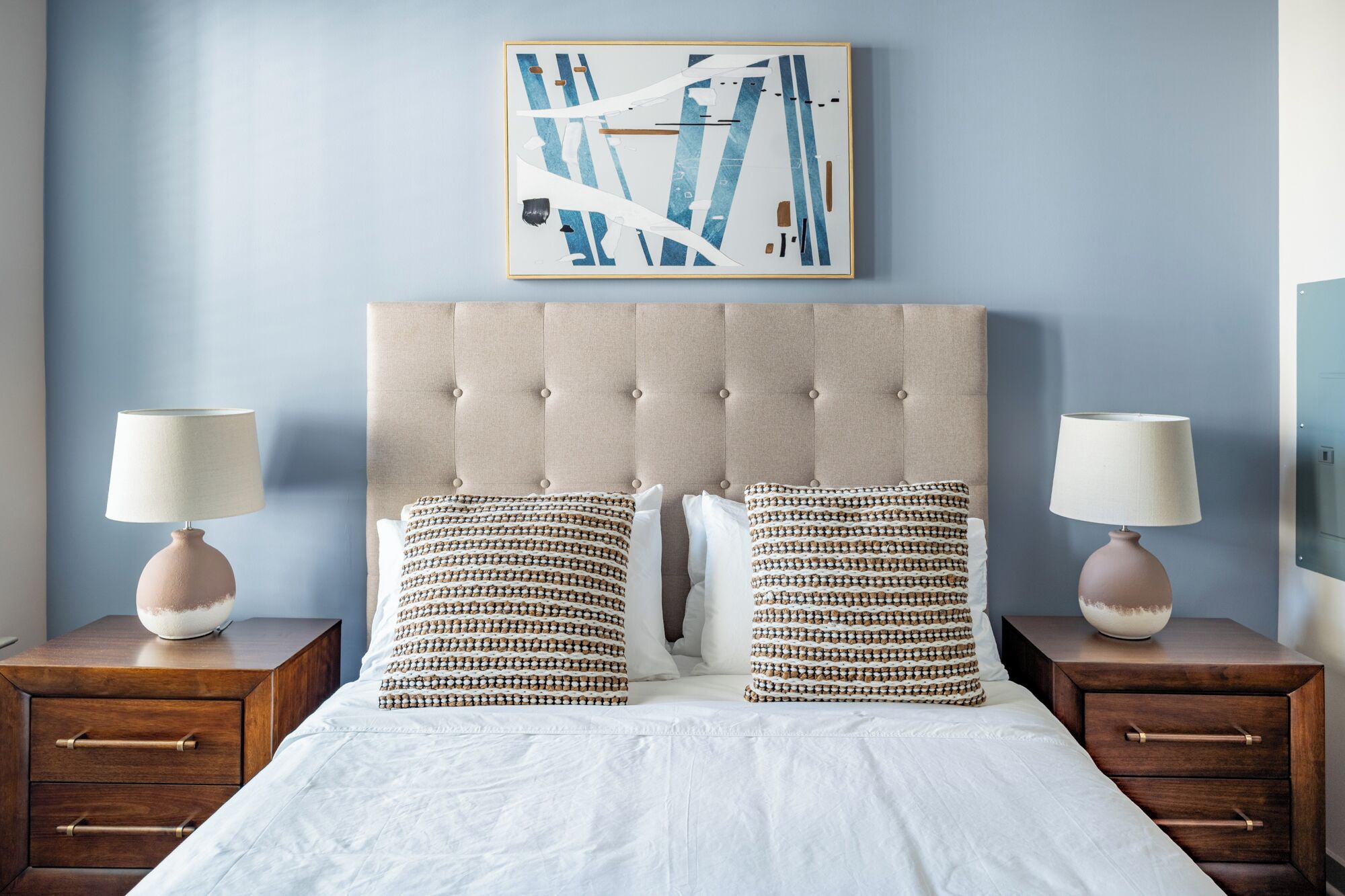 A bedroom with a tufted headboard, two bedside tables with lamps, and patterned pillows.
