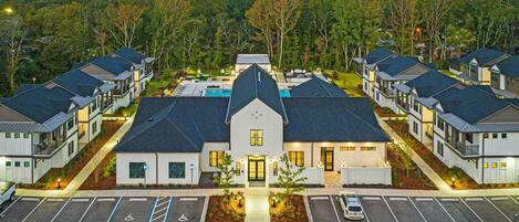 A modern hotel with a central building and symmetrical wings, featuring a parking lot and landscaped areas.