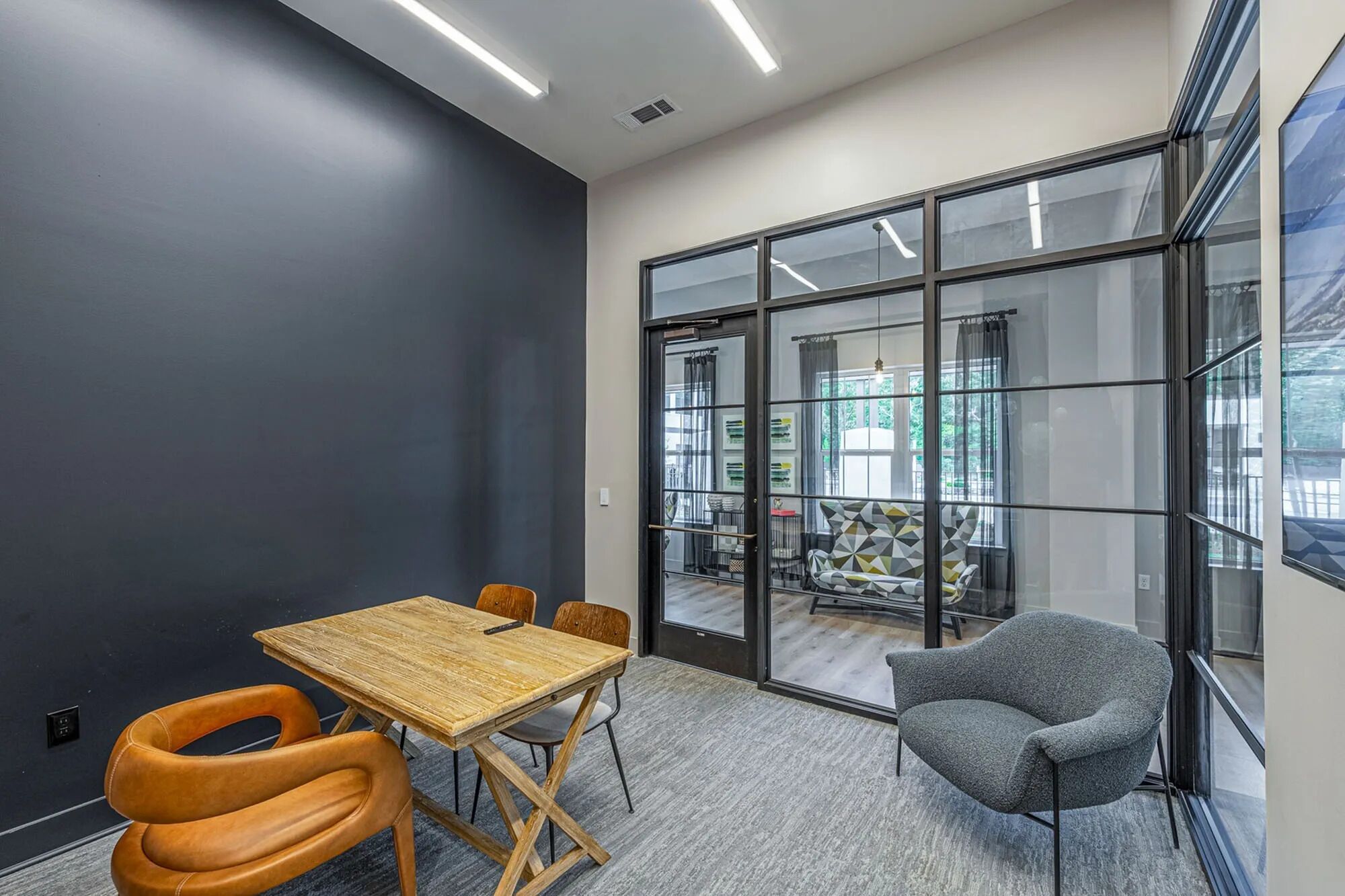 A modern meeting room with a wooden table, leather chairs, and a grey armchair.